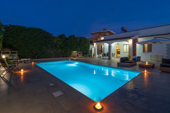 Une piscine avec un espace patio, du mobilier d’extérieur et une maison en arrière-plan.