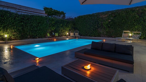 A swimming pool with a sunken seating area, surrounded by lounge chairs and a covered umbrella. - Villa 'Villa Gioia Fontane Bianche' with Sea View, Wi-Fi and Air Conditioning (Siracusa)