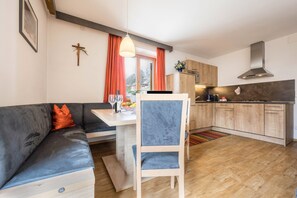 A modern kitchen with wooden cabinets, a dining area with a blue chair, and a gray sofa with orange pillows.