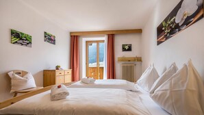 Camera d'albergo con due letti, una testiera e un comò in legno, un termosifone e una finestra con tende.