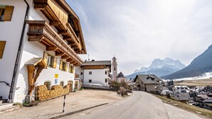 Una calle con balcones de madera tradicionales, una iglesia con campanario y montañas al fondo.
