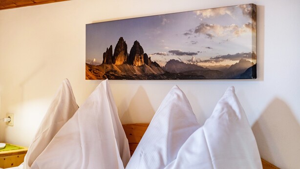 Una cama con almohadas blancas y un cuadro de un paisaje montañoso en la pared.