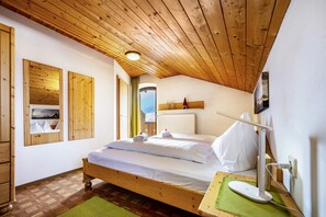 Un plafond en bois, un lit avec du linge de maison blanc, une table de chevet avec une lampe, et une vue sur le ciel par la fenêtre.