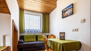 Una habitación con techo de madera, una ventana con cortinas verdes, un sofá con cojines verdes, una silla de madera y una mesa con mantel verde.
