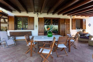 A covered patio with a dining table, wooden chairs, and a wicker sofa.
