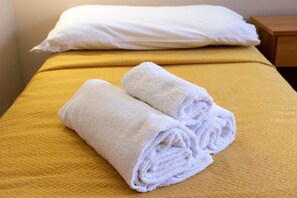 Ein Bett mit einer gelben Bettdecke und zwei aufgerollten weißen Handtüchern.