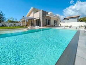Et moderne hus med swimmingpool, overdækket terrasse og hvid facade.
