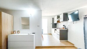 Une cuisine moderne dotée d’un téléviseur à écran plat, d’un plan de travail blanc et d’un revêtement de sol en bois.