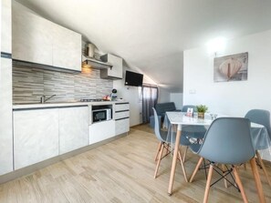 Une cuisine moderne équipée d’un four et d’un micro-ondes intégrés, un coin repas avec une table et des chaises, et un téléviseur à écran plat fixé au mur.