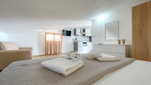 Une chambre à coucher avec un lit, une chaise, un téléviseur et, au fond, une cuisine.