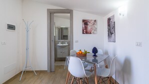 A dining area with a glass table, white chairs, a basket of fruit, and artwork on the wall. - 'Nord in Villa Sele' Apartment with Shared Pool, Wi-Fi, and Air Conditioning (Fontane Bianche)
