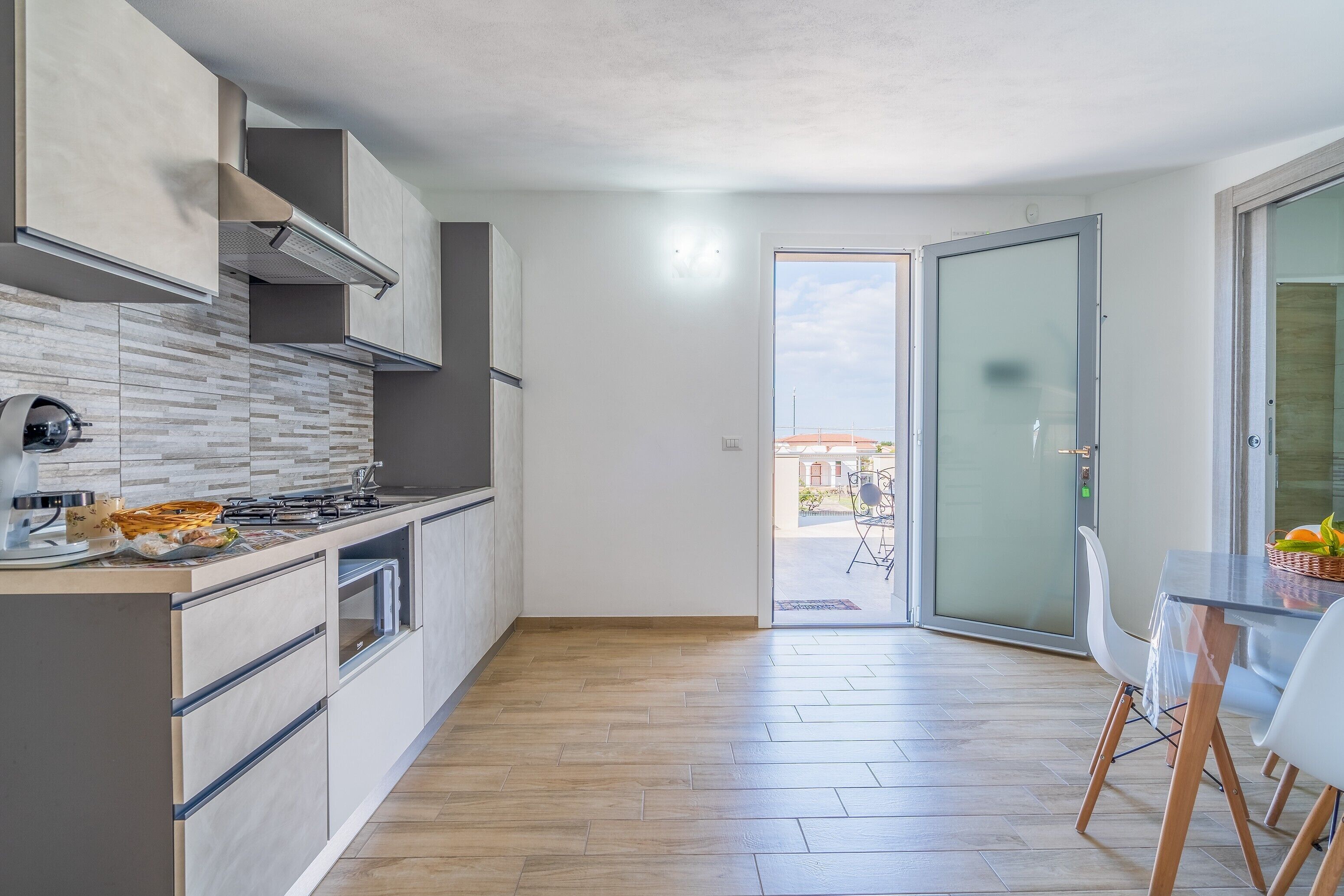 A modern kitchen with a large island, a dining area with a glass table, and a sliding glass door leading to an outdoor patio.
