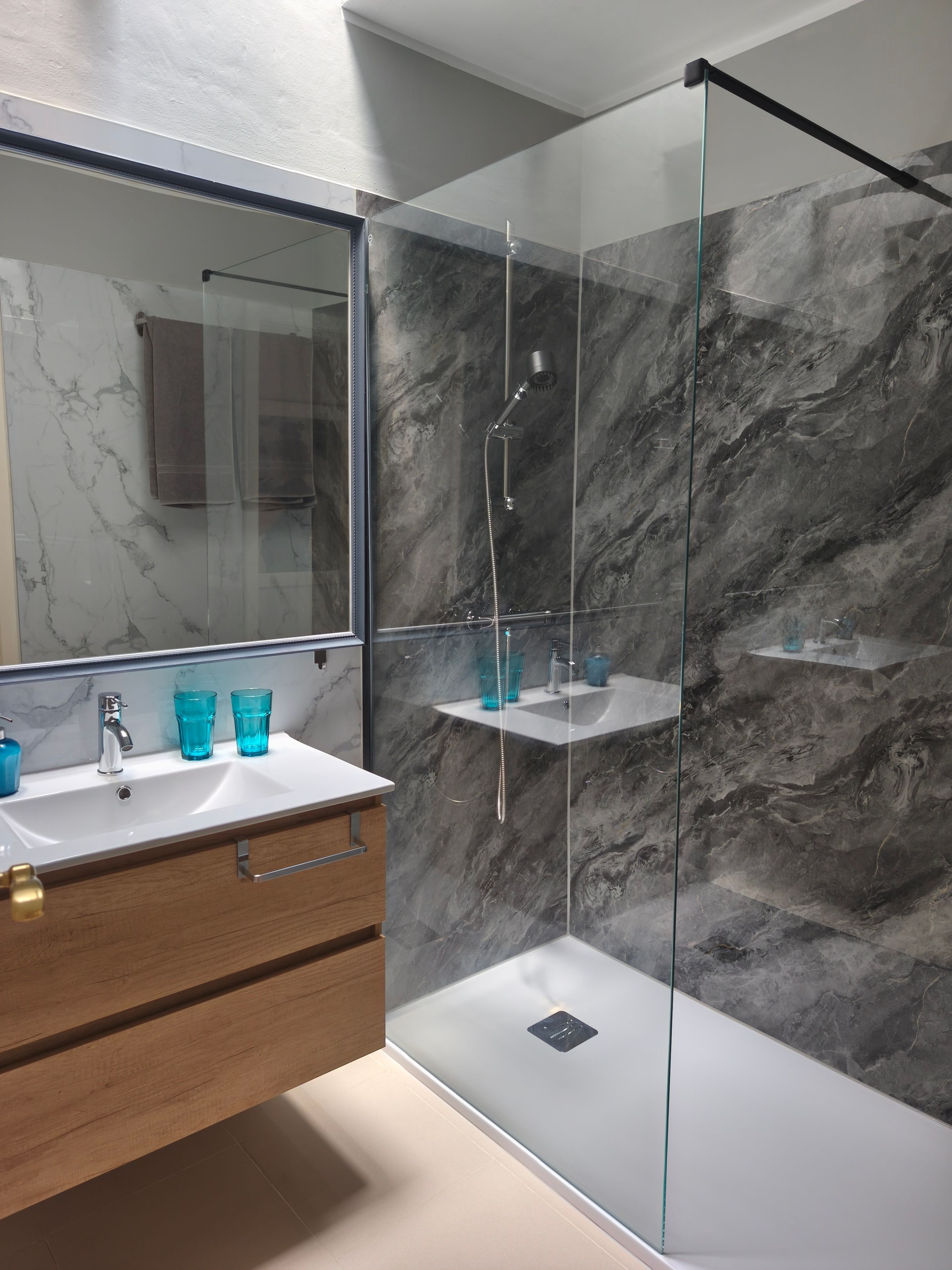 A modern bathroom with a glass-enclosed shower, marble walls, a wooden vanity, and a large mirror.