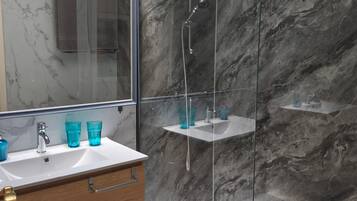 A modern bathroom with a glass-enclosed shower, marble walls, a wooden vanity, and a large mirror.