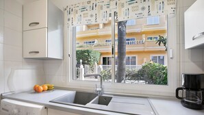 Una cocina con lavadora, un lavamanos y un ventanal con vistas a un edificio y vegetación.