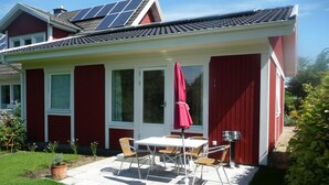 Ein rotes Haus mit einer überdachten Terrasse, Solaranlage und Garten.