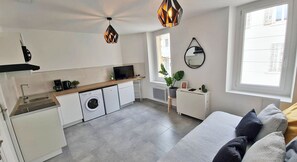 A modern kitchen with a washing machine, a TV, and a dining area with a sofa.