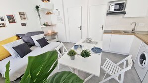 Un espacio habitable compacto con sofá, mesa de comedor, sillas, pequeña cocina con microondas y lavadora.