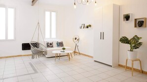 Una habitación moderna y luminosa con una lámpara colgante, un sofá blanco con cojines estampados, una mesita redonda y una planta en maceta.