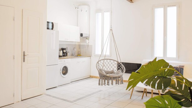 Una cocina moderna con armarios blancos, lavadora y una silla colgante.