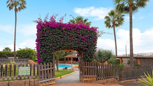 Una verja de madera con un letrero, un área de piscina y un pérgola con flores moradas.