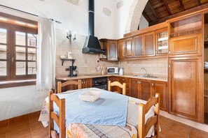 A kitchen with wooden cabinets, a dining table with chairs, a microwave, and a black stove hood.