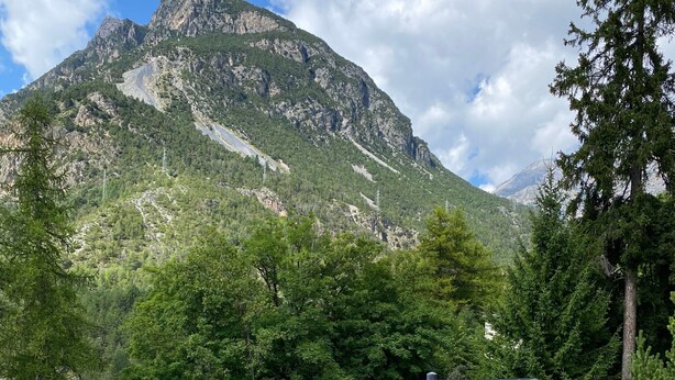 Eine Berglandschaft mit einer Holzhütte, einem gepflasterten Weg und einem eingezäunten Bereich.