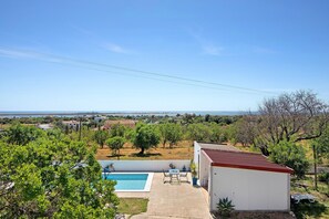 Une piscine avec un patio, un petit bâtiment blanc et une vue sur la campagne.