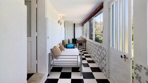 Ein Korridor mit Schachbrettmuster, einem Bett mit Kissen, einem Schreibtisch mit Stuhl und einem Fenster mit Blick.