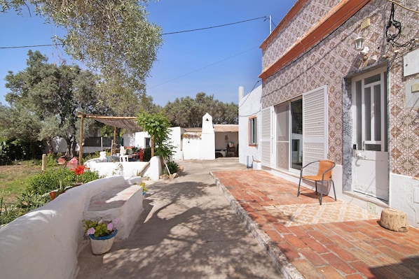 A courtyard with a brick pathway, a white building with a tiled facade, and a wooden pergola.