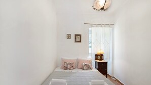 A bedroom with a bed, pillows, a bedside table with a lamp, and a window with curtains.