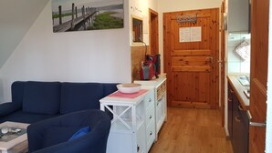 A cozy living room with a dark blue sofa, a small white table with a bowl, and a painting of a pier on the wall. - Vacation apartment 03 for friends (Zinnowitz)