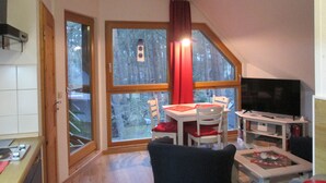 A cozy living room with a dining area, large windows, a TV, and a fireplace. - Vacation apartment 03 for friends (Zinnowitz)