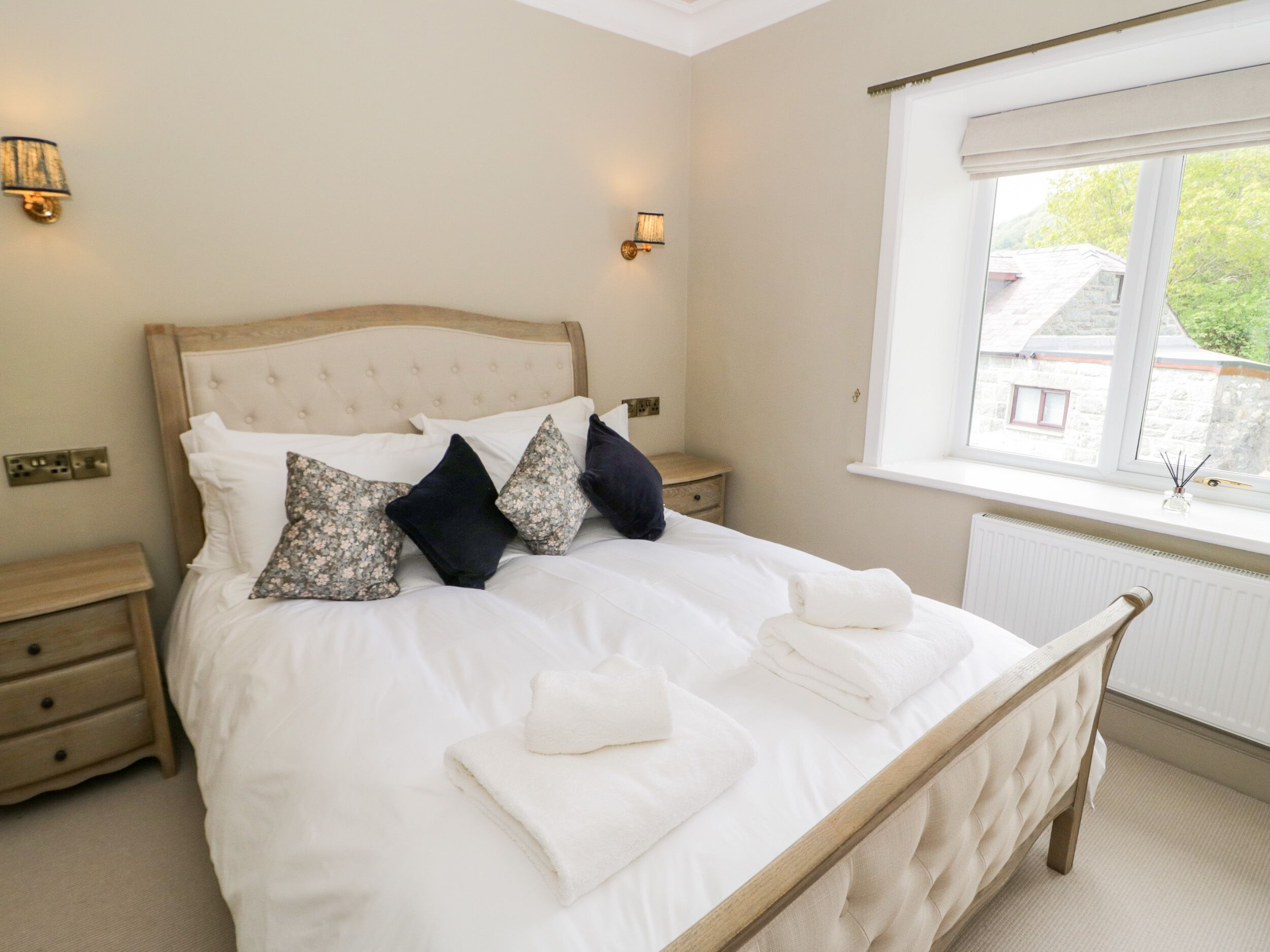 A neatly made bed with white linens and decorative pillows, a wooden headboard, and a window with a view of buildings outside.