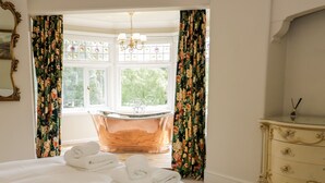 A bedroom with a large bed, a bathtub, and a dresser. - Gwern Borter Manor (Conwy)