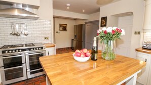 A kitchen with a wooden countertop, a bowl of apples, a bottle of champagne, and a vase of flowers. - Gwern Borter Manor (Conwy)