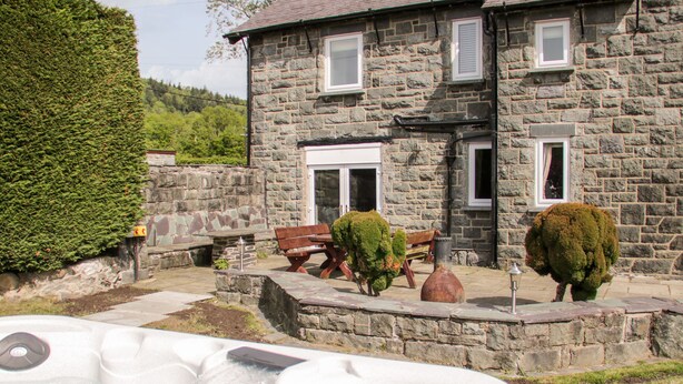 A stone building with a hot tub, benches, and neatly trimmed bushes. - Gwern Borter Manor (Conwy)