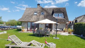 Een huis met rieten dak, een terras met tuinmeubilair en een gazon.