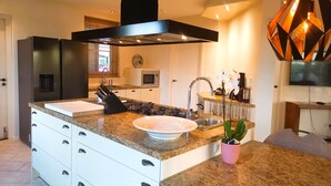 Een moderne keuken met een centraal eiland, roestvrijstalen apparatuur en een hanglamp.