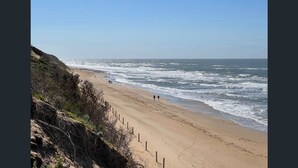 A beach with a sandy shore and waves crashing onto it. There are a few people walking along the beach. - Roadknight Ocean Road View 236 400m to Beach (Anglesea)