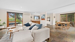 A spacious living room with a sofa, a dining table, and chairs. There is a kitchen area in the background. - Roadknight Ocean Road View 236 400m to Beach (Anglesea)