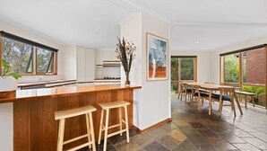 A modern kitchen with a wooden island, bar stools, and a dining area with a table and chairs. - Roadknight Ocean Road View 236 400m to Beach (Anglesea)