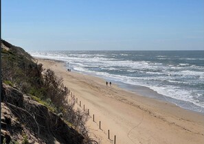 A beach with a sandy shore and waves crashing onto it. There are a few people walking along the beach.