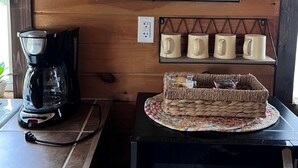 Pared de madera con un reloj, contenedores de acero inoxidable, una cafetera y una cesta sobre una mesa.