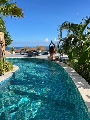 Une piscine d’un bleu éclatant, à bords incurvés, entourée de plantes tropicales et offrant une vue sur l’océan.