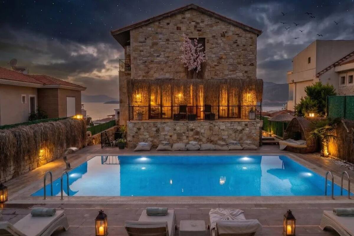 A stone building with a pool, outdoor seating, and a view of the sea.