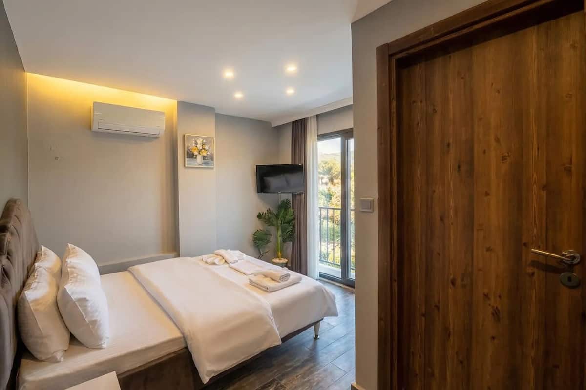 A bedroom with a bed, a TV, a wooden door, and a window.