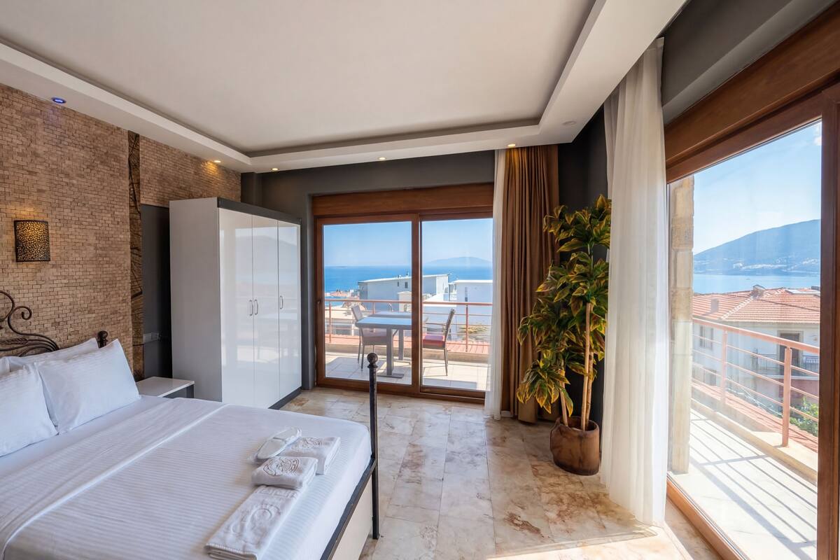 A hotel room with a bed, a wardrobe, a balcony with a view of the sea, and a potted plant.