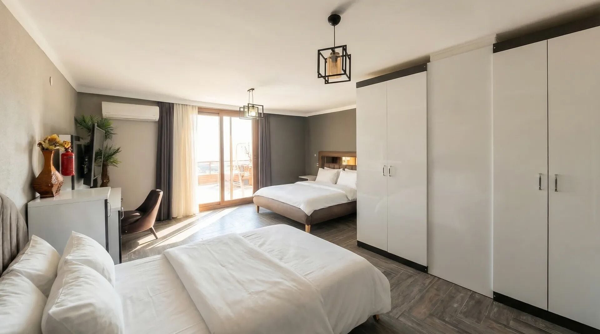 A hotel room with a bed, a desk, a chair, a wardrobe, and a sliding door to a balcony.