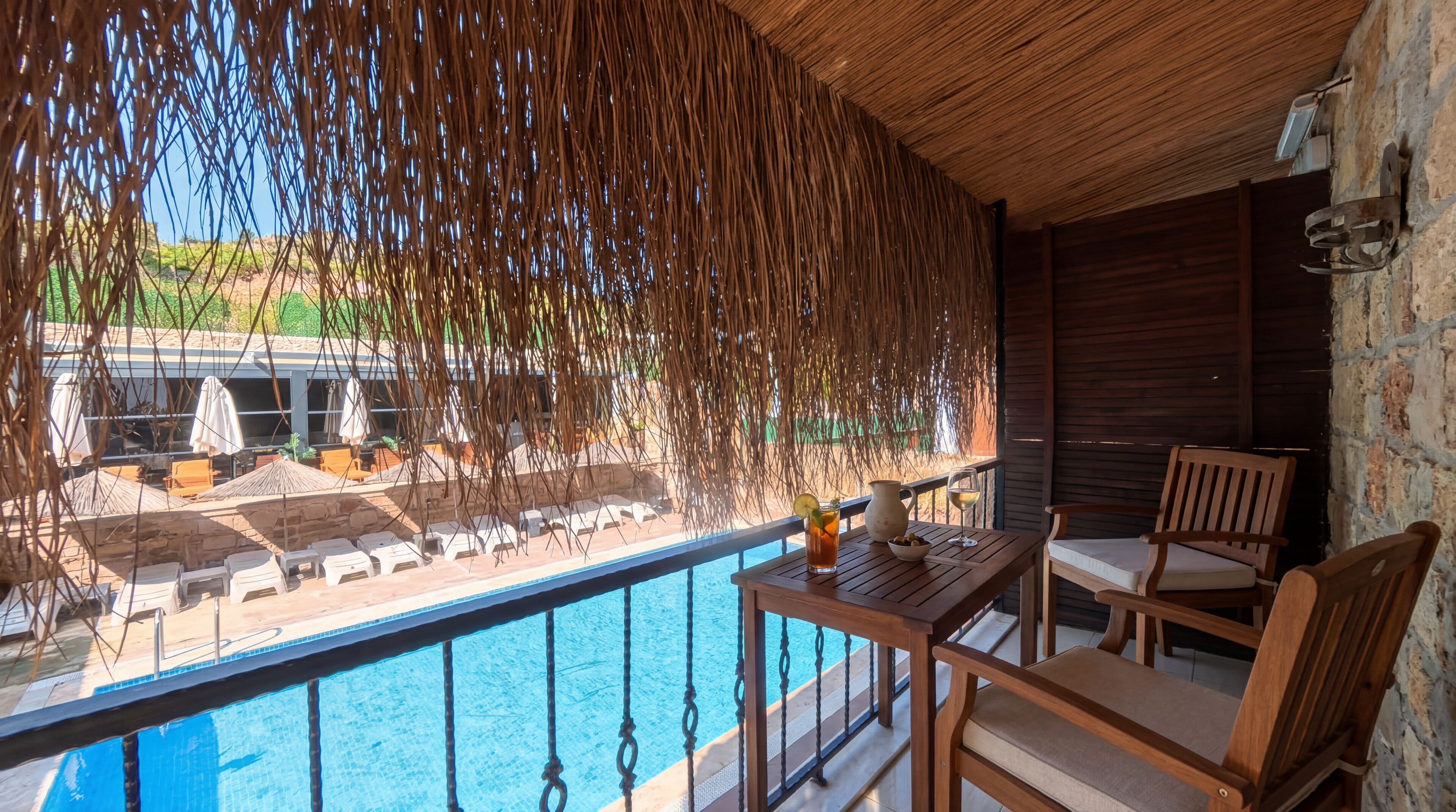 A balcony with a pool, wooden furniture, and a view of the pool area.